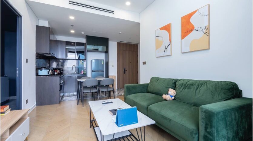 Tổng quan phòng khách và bếp căn hộ Lumiere Riverside Tháp West với sofa nhung xanh và tranh trừu tượng | Living room and kitchen overview of Lumiere Riverside West Tower apartment with green velvet sofa and abstract paintings